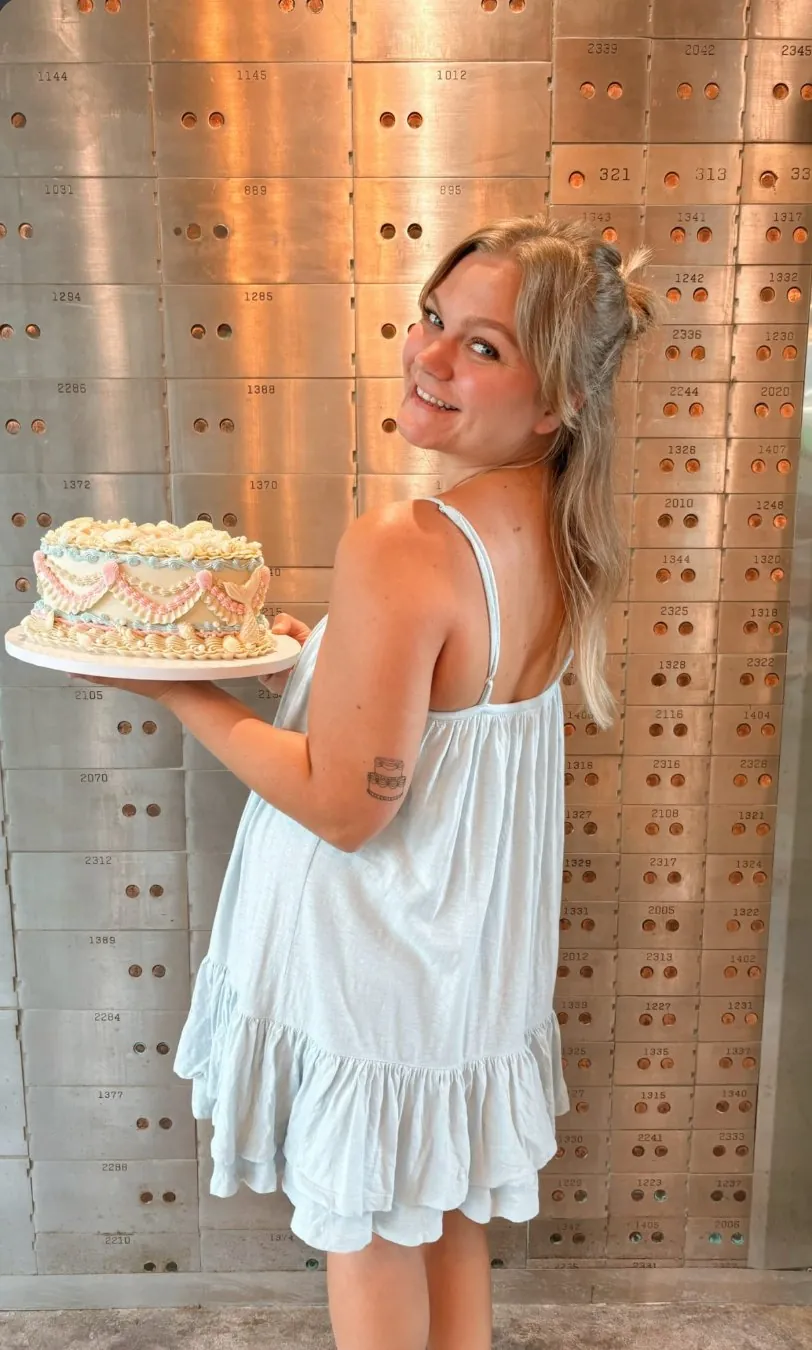 Kennedy McDuff holding a vintage piped cake in front of a wall of bank vault boxes