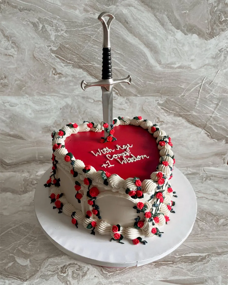 Red-topped heart cake with tiny piped roses and a sword topper