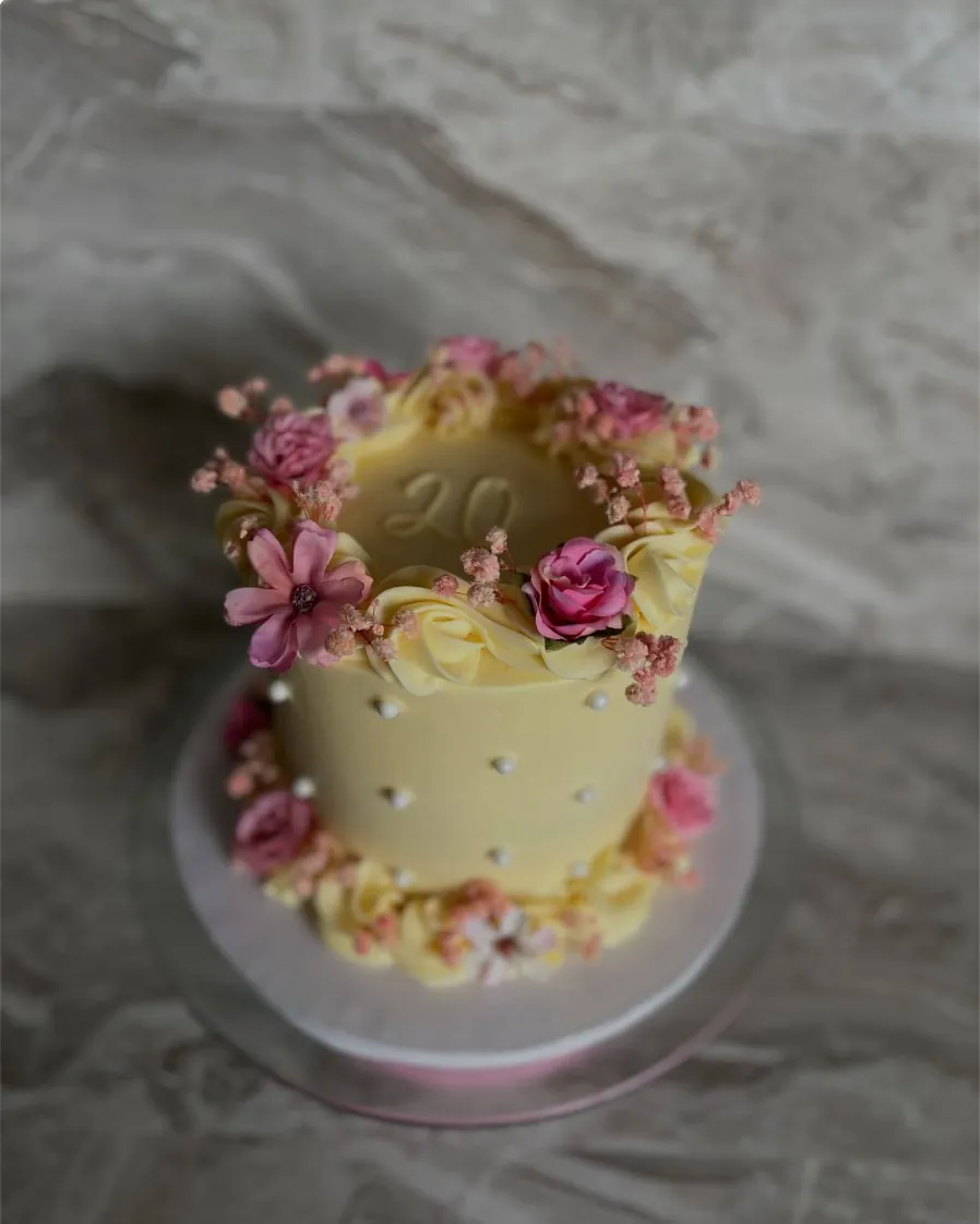 Buttercup yellow 20th birthday cake ringed with pink roses and baby's breath